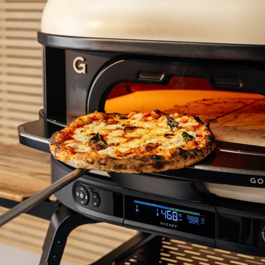 Pizza op een schep uit de Gozney Dome, met de vlam achteraan